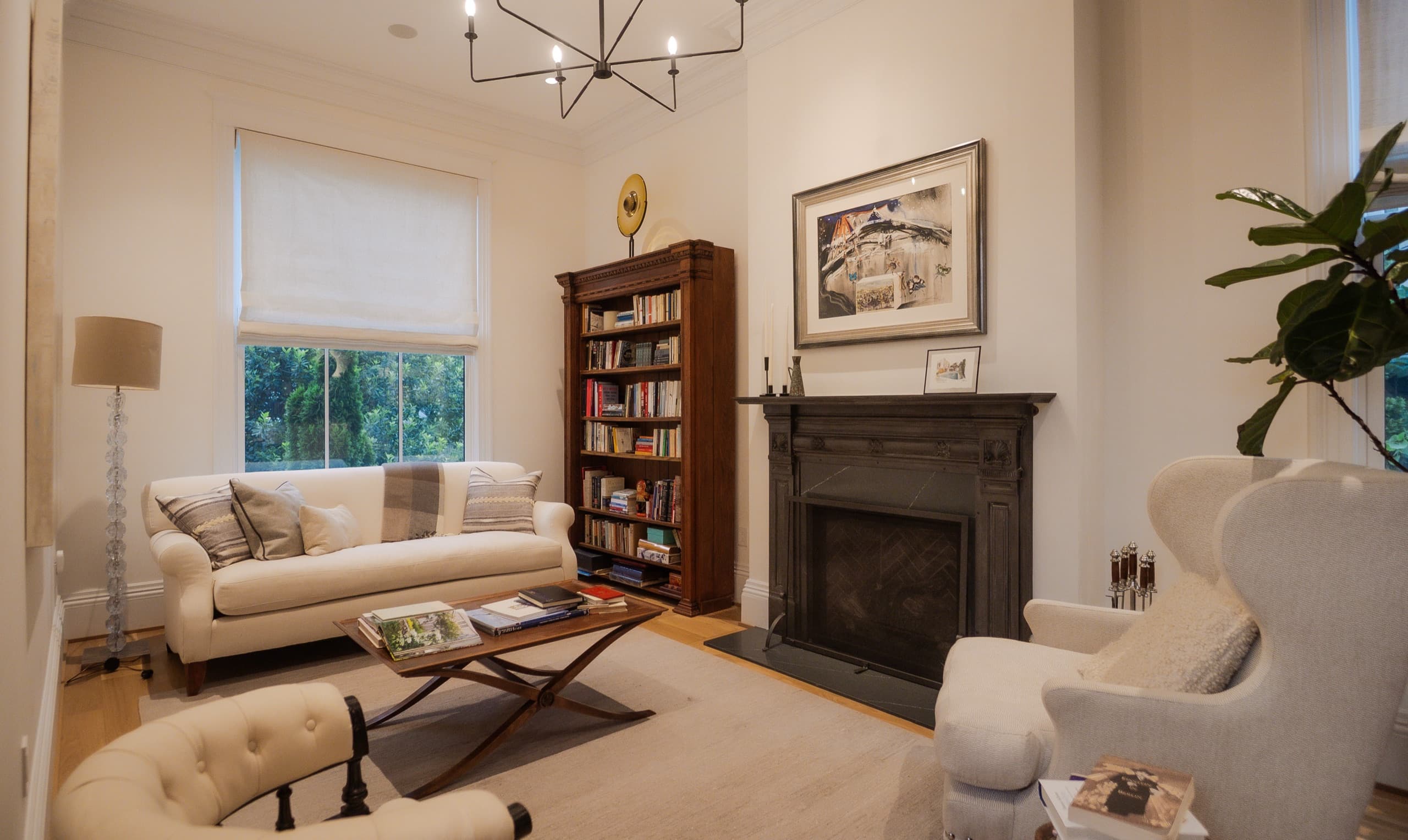 Sitting room with a dark stone fireplace, timber bookcase and a branched ceiling light