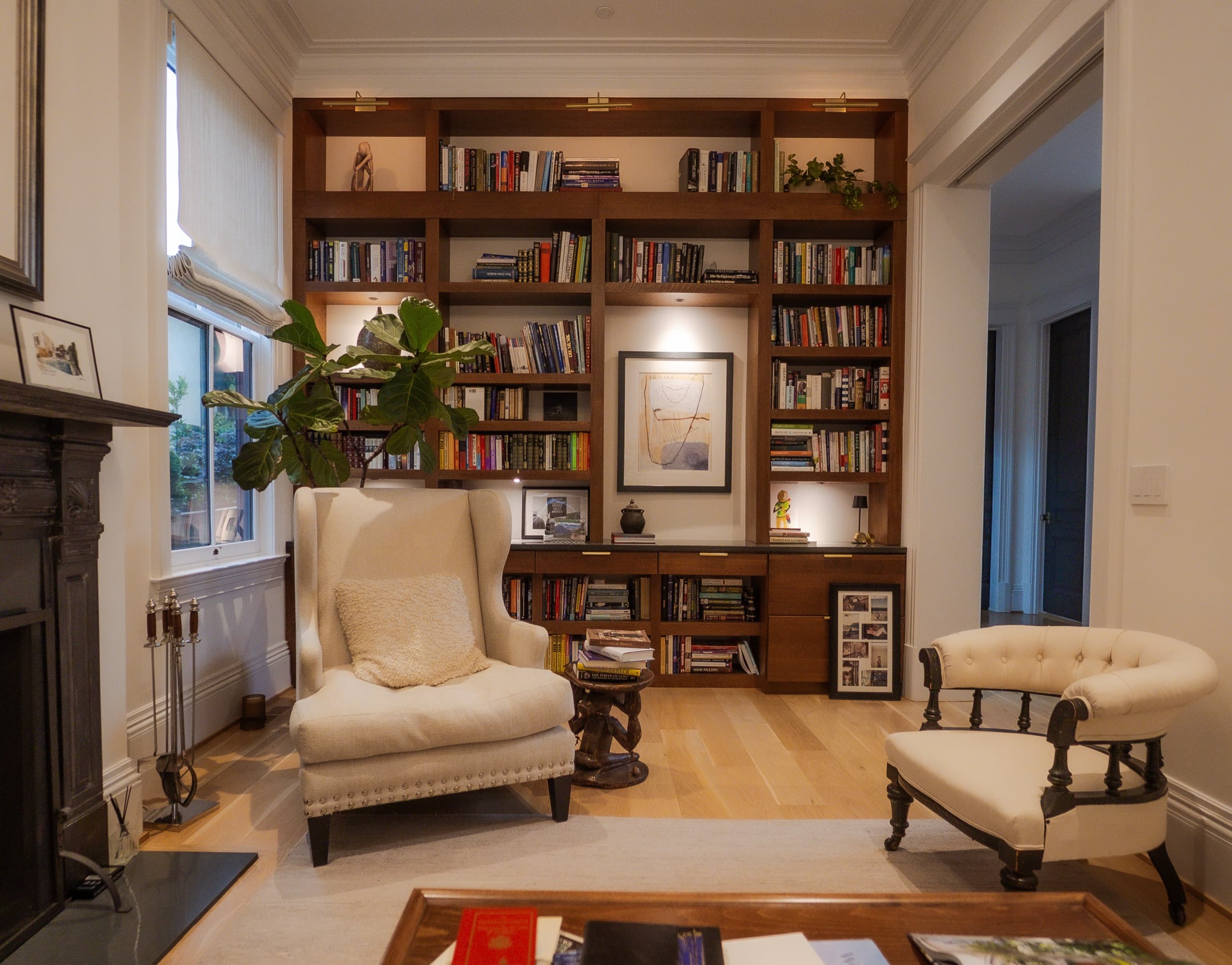 Library wall of lit walnut bookshelves, with a wing chair and carved side table