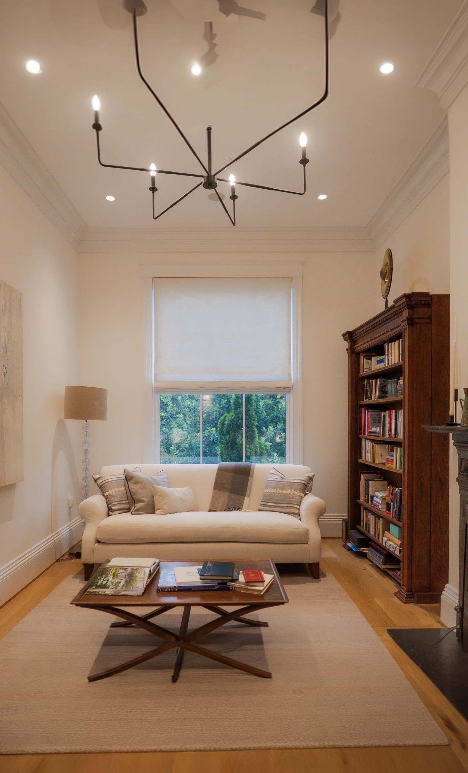 Formal sitting room with a branched pendant, roman blind and a tall antique bookcase