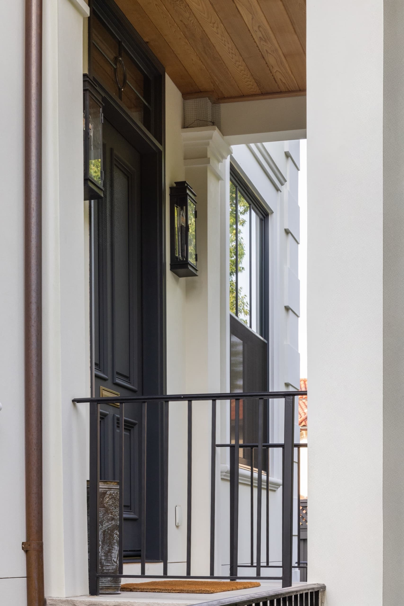 Front porch detail with a black panelled door, timber soffit and a wrought-iron railing